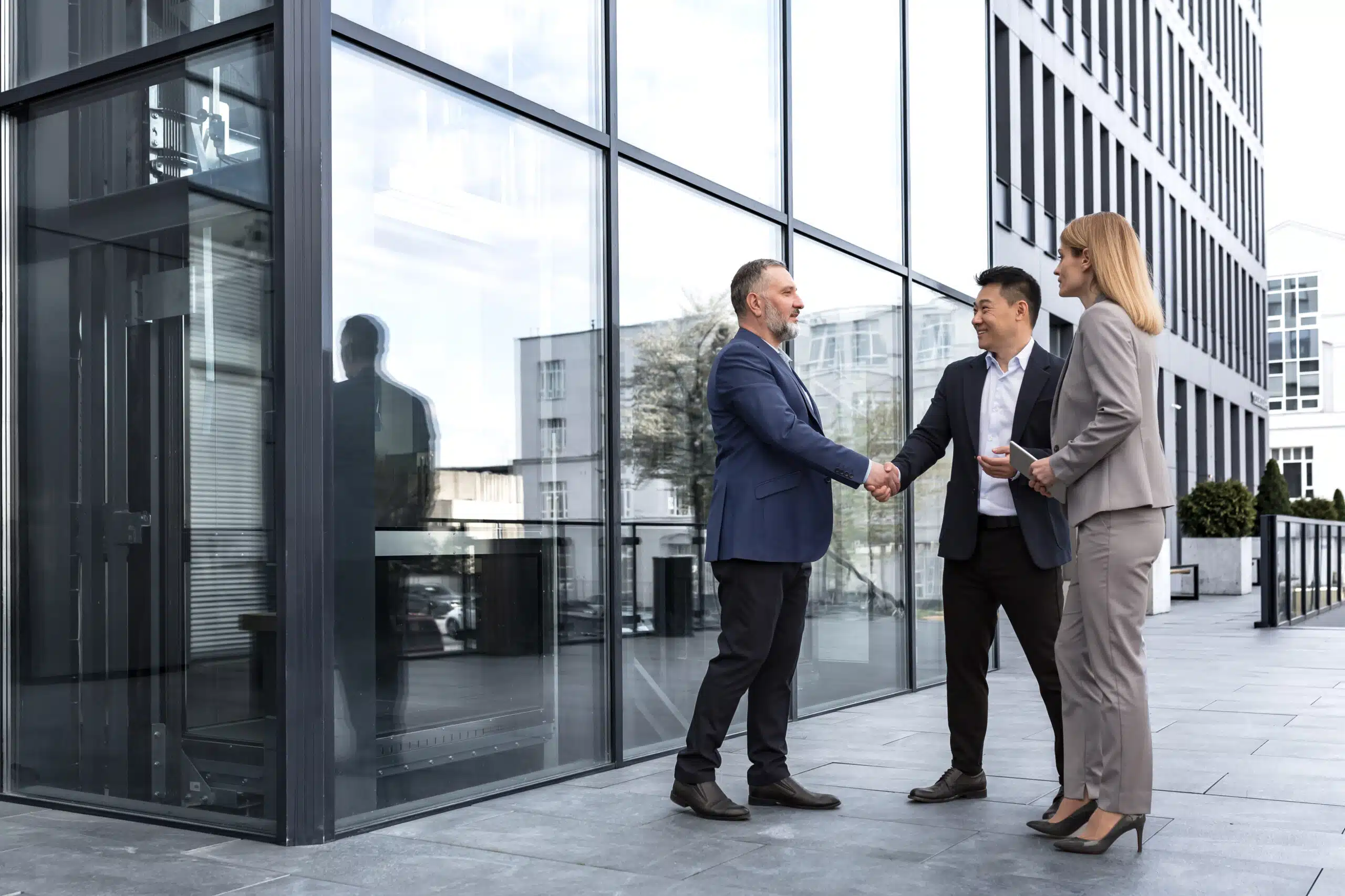 Audit team shaking hands outside of an office building confidently equipped with a tablet