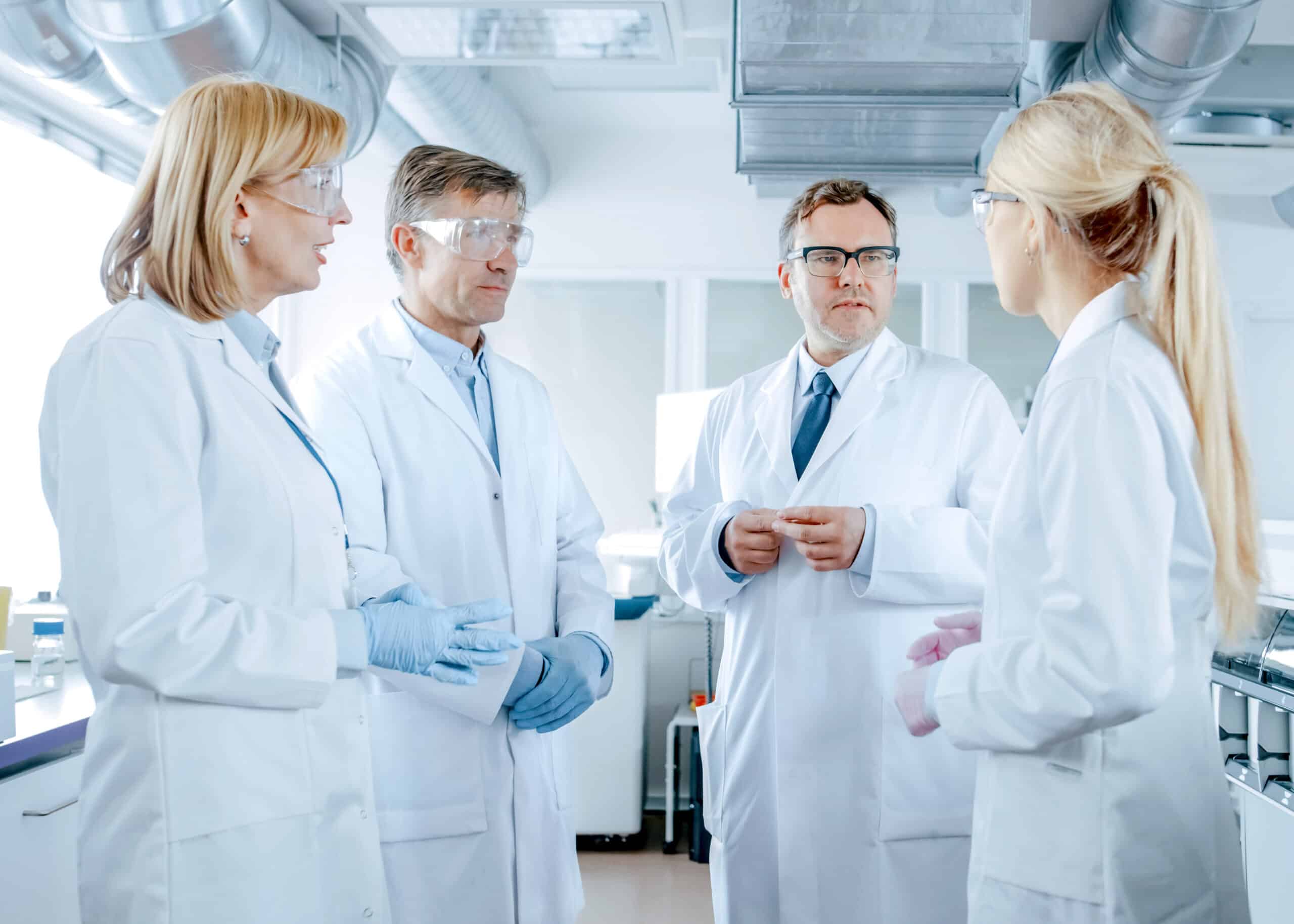 A group of workers in lab gear in a circle to discuss a complaint