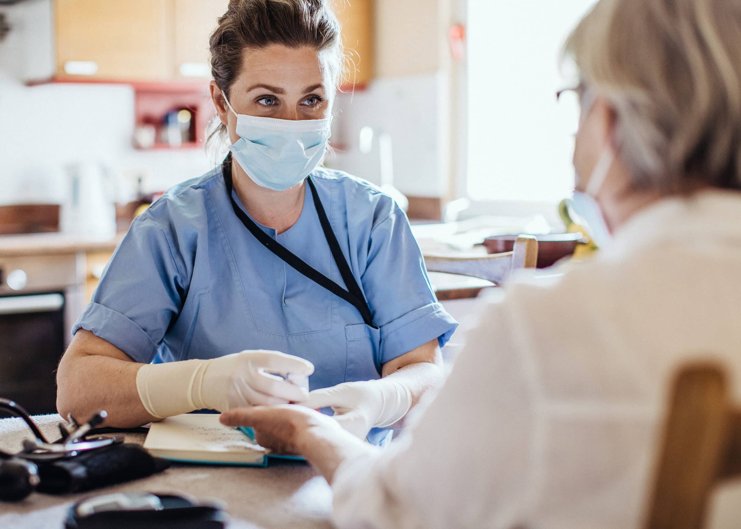 A doctor in personal protective gear talking to a patient and writing down notes