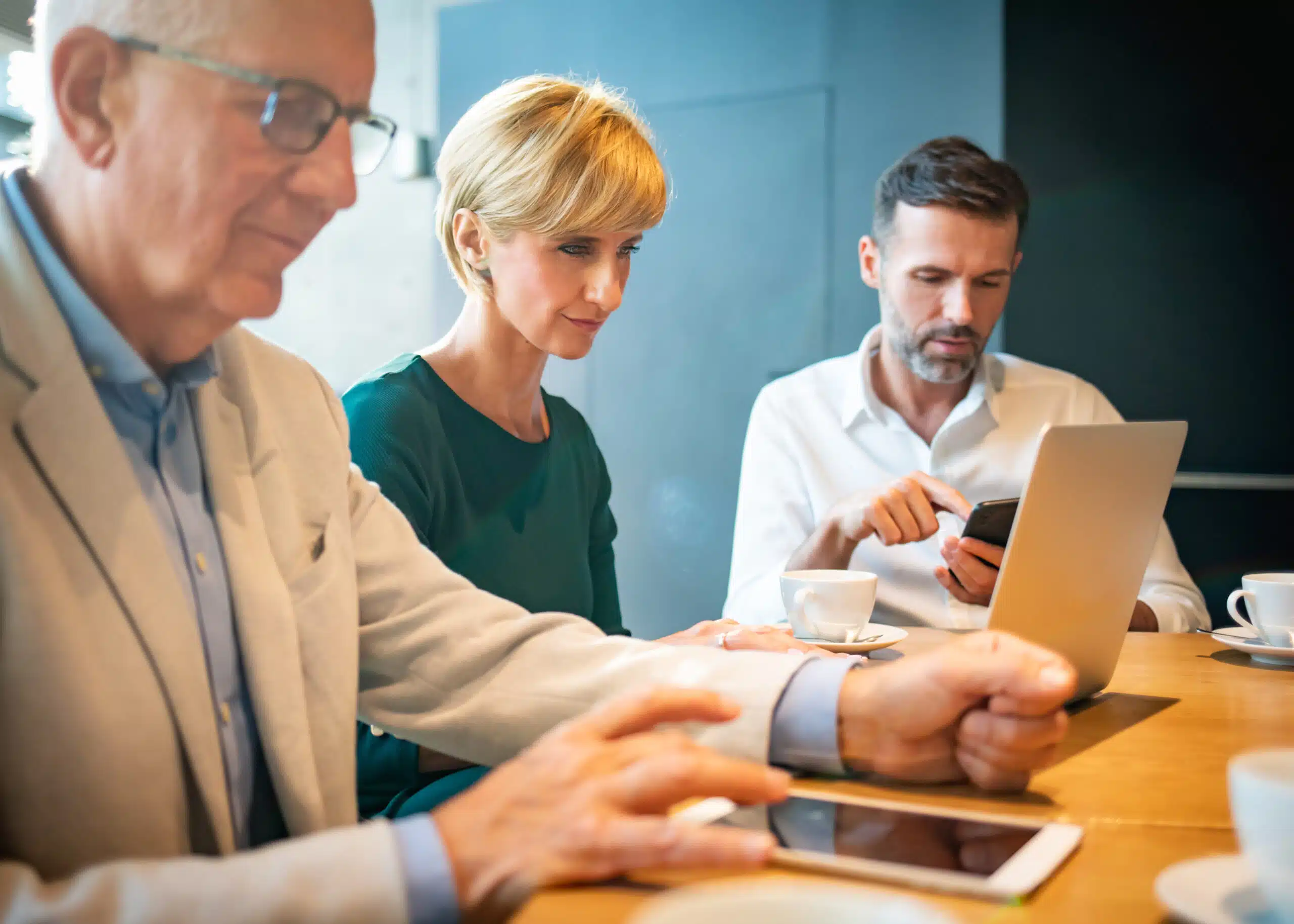 Three coworkers collaborating on a tablet, phone and laptop to triage complaints