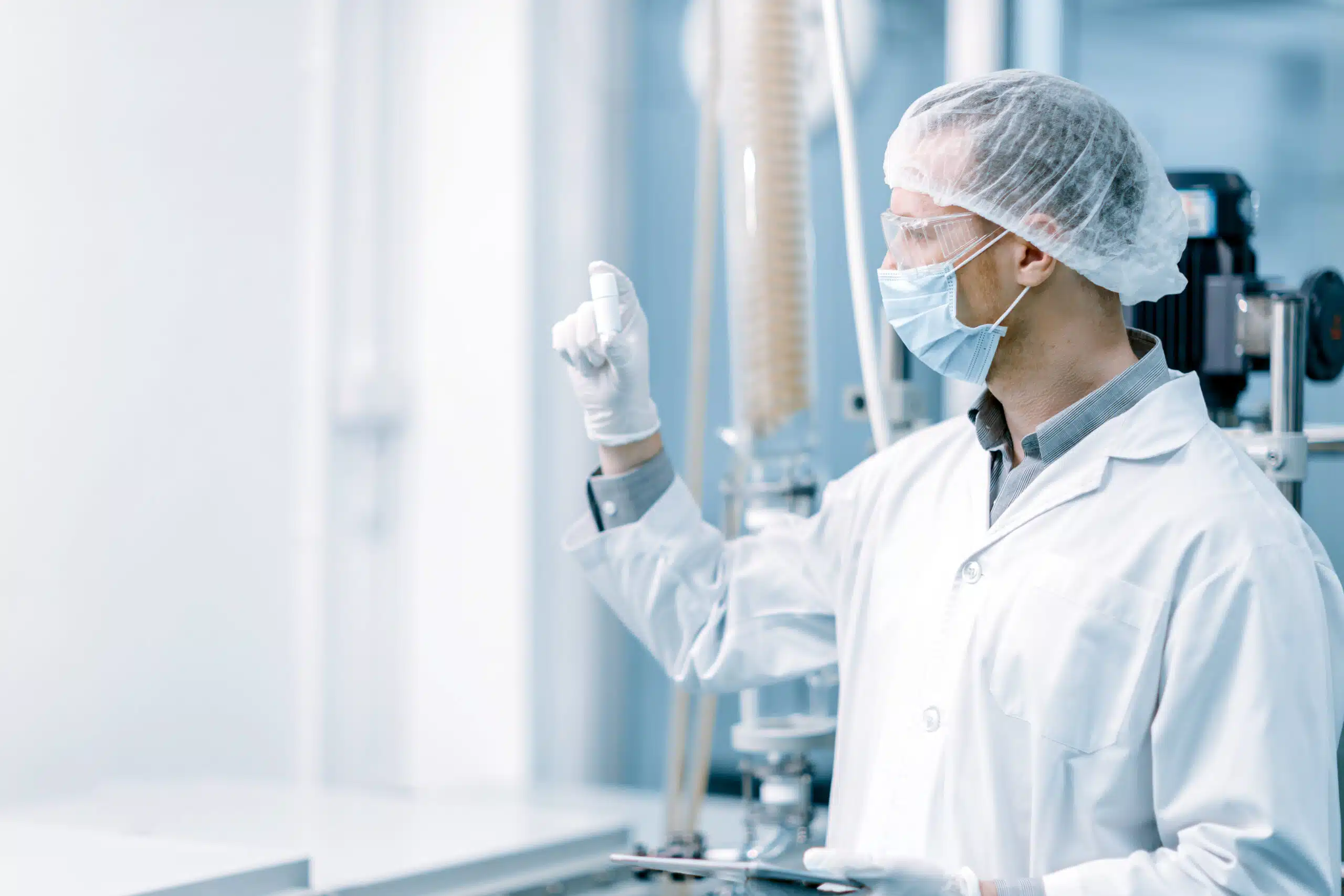 A worker in personal protective gear investigating the quality of a small white object