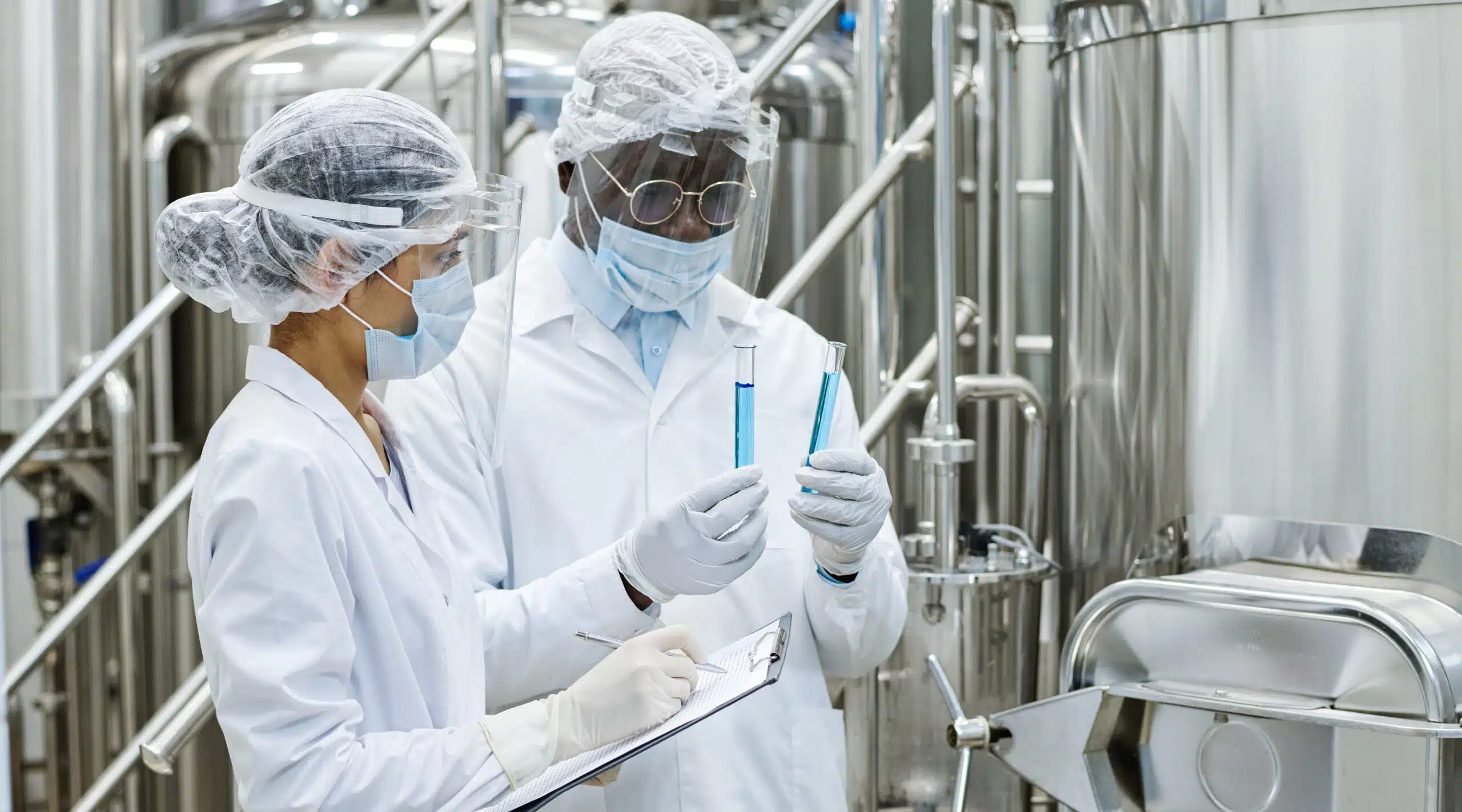 Two workers in personal protective gear comparing the quality of two similar tubes to see which is better