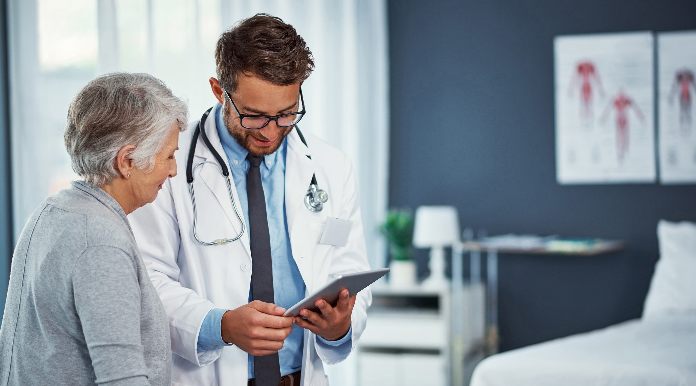 A doctor smiling and sharing clear digital information with a smiling patient with a tablet