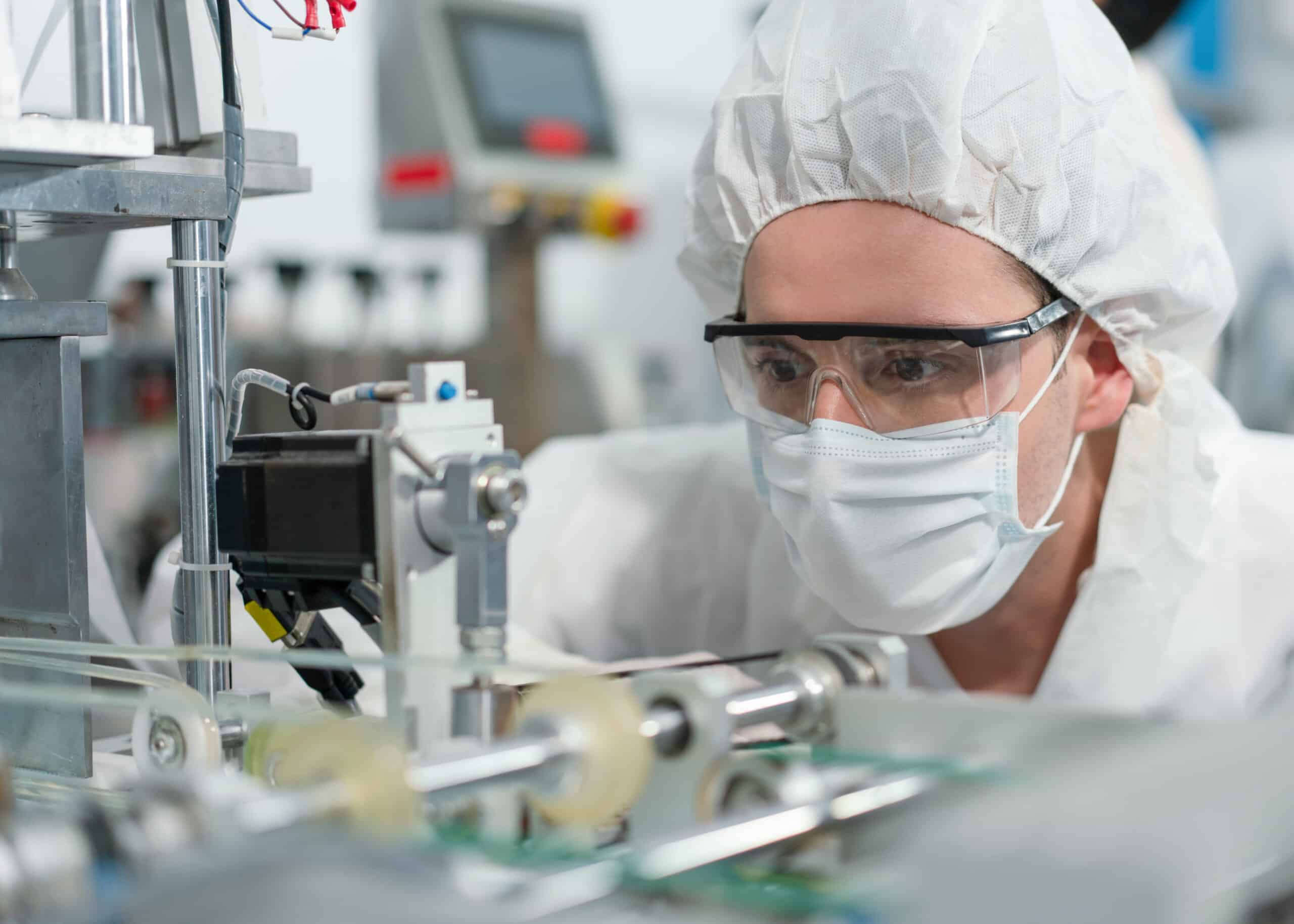 A man in personal protective equipment closely observing medical device production machinery