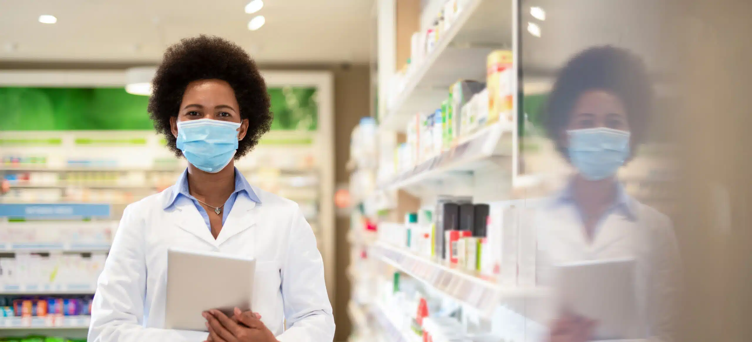 A woman in a pharmacy holding a tablet facing the camera