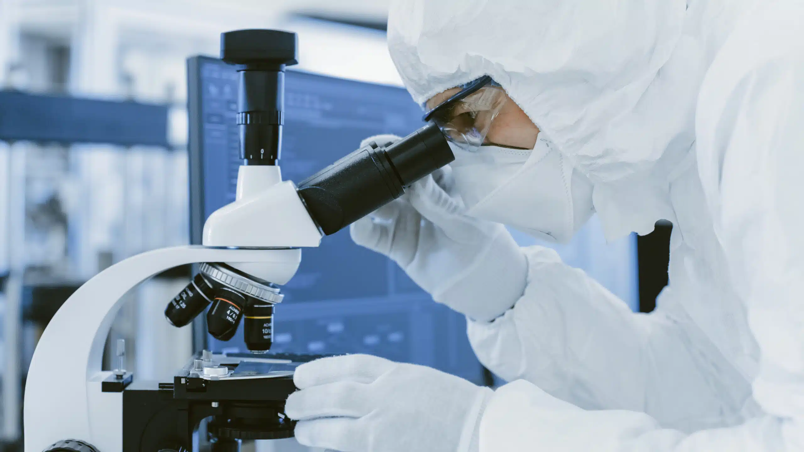 Worker in personal protective equipment using a microscope to investigate a batch out of specification