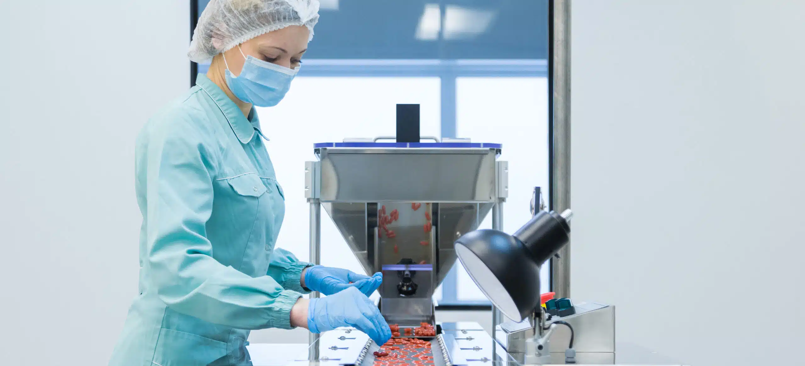 A woman in personal protective gear inspecting a batch of pills on a conveyer belt for an Out of Specification (OOS) investigation