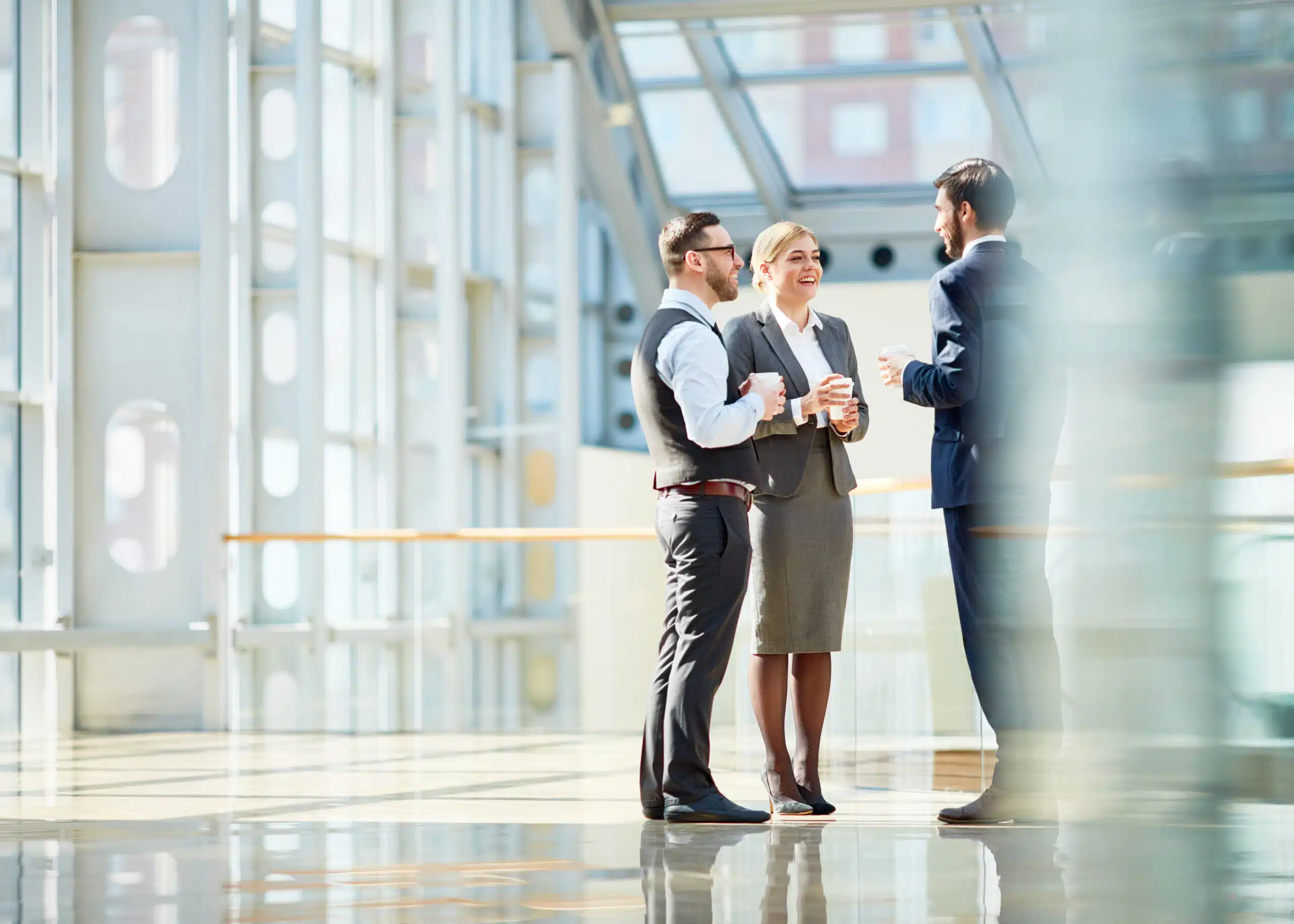 Three people in business suits meeting to discuss audits in a lobby