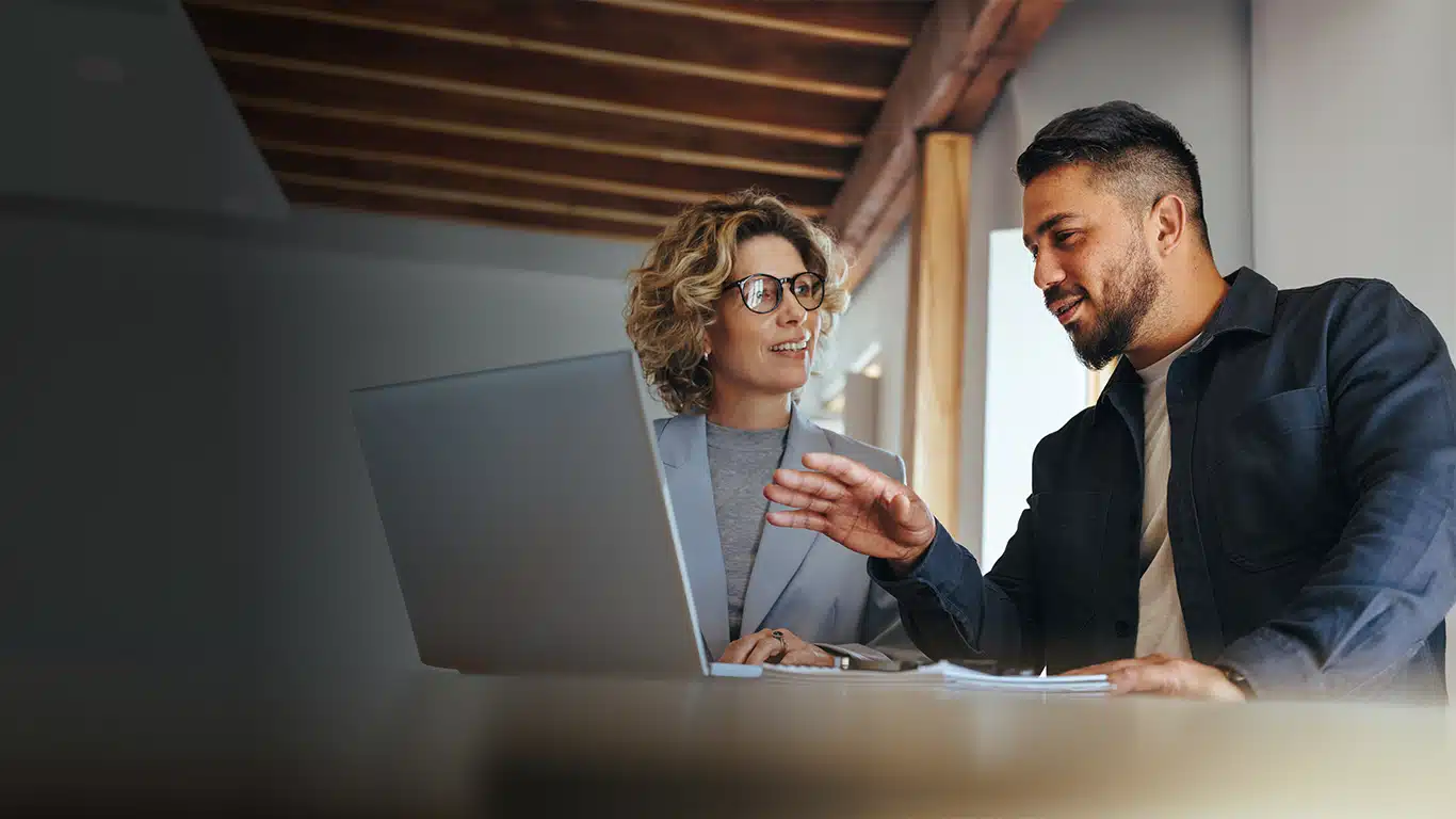 Two professionals sharing a laptop on a table to view ai enabled QMS software