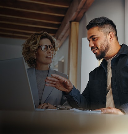 Two professionals sharing a laptop to look at ai enabled QMS software