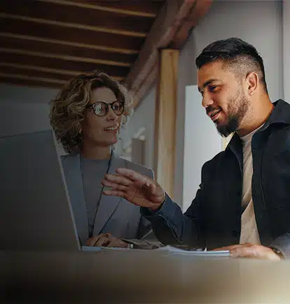 Two professionals sharing a laptop to look at ai enabled QMS software